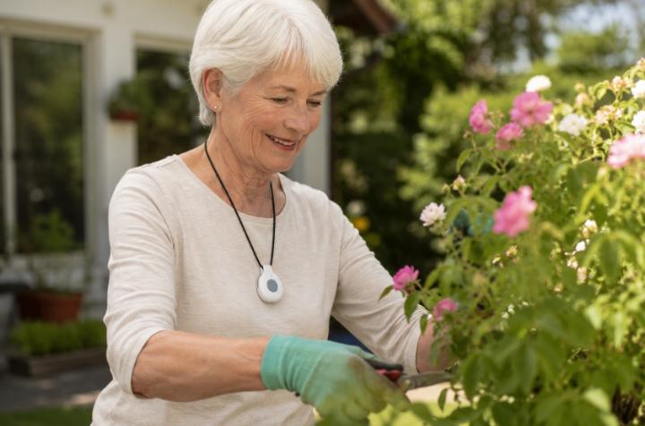 Senior woman wearing a discreet medical alert pendant while doing light gardening — natural, not clinical
