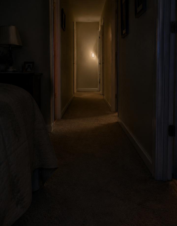 A dim apartment hallway at night with one light switch far from the bedroom door, shown from a low nighttime perspective