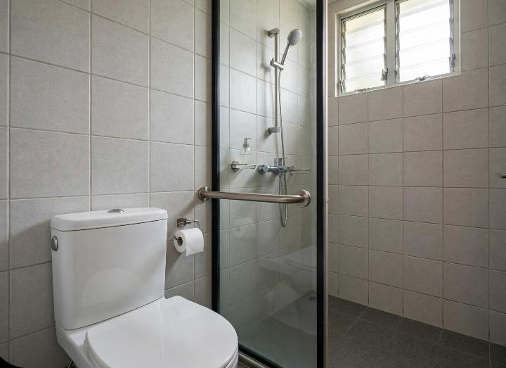 a stainless steel grab bar mounted on a bathroom wall beside a toilet and inside a shower stall, HDB flat bathroom style tiling, soft natural lighting, no people, clean and modern, shot at eye level"