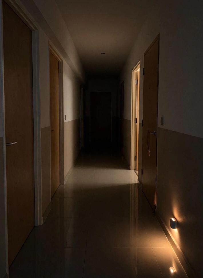 photo of a dim HDB flat hallway at night with a small motion sensor LED night light glowing near the floor skirting, warm ambient light, no people, cozy but slightly dark atmosphere